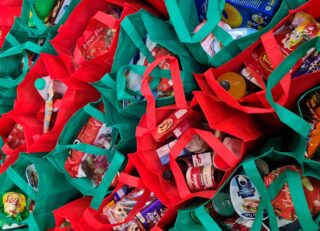 Dozens of red and green tote bags full of groceries and lined up.